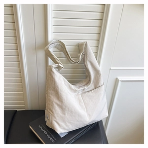Detail of adjustable wide shoulder strap and front pocket on off-white nylon tote bag