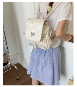 Detail of a beige leather backpack with a silver butterfly clasp and soft butterfly prints