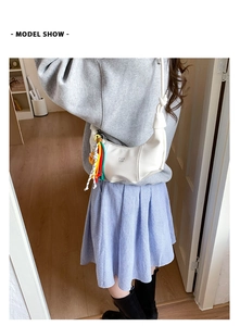 Side view of a white crescent moon shoulder bag with colorful braided tassel charm