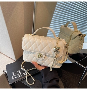 Macro detail of creamy white quilted bag with golden ball chain and lock mechanism