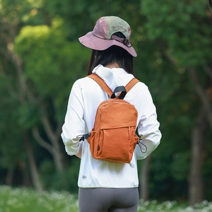 Close-up of orange mini nylon backpack with side drawstring on a model outdoors