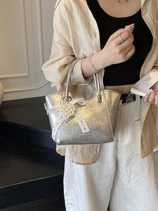 Silver metallic bucket bag with pearl heart charm and lace ribbon detail in a street setting