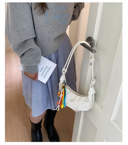 Detail of white moon bag featuring knotted strap, brand logo, and colorful tassel charm
