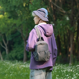 Outdoor shot of a compact dark grey waterproof nylon backpack worn by a model