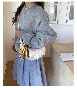 Detail of white PU dumpling bag with pleats, brand lettering and colorful rope charm
