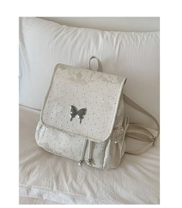 Detailed view of floral embroidery and silver butterfly metal clasp on cream backpack