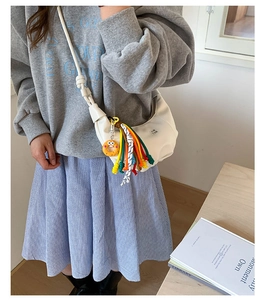 Detailed shot of white crescent crossbody bag with colorful tassels and donut charm decor