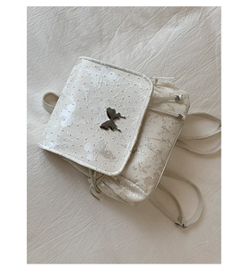 Détail de la texture en dentelle florale blanche et logo papillon argenté du sac