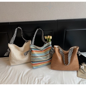 Detailed view of three large woven straw shoulder bags in white, rainbow, and brown colors