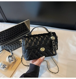 Close-up of black quilted leather bag with gold clasp and chain on white sheets