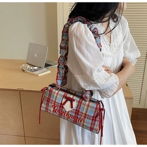 Detail of red and blue checkered shoulder bag featuring heart patch and bow on frill strap