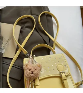 Detail of light yellow leather crossbody bag with rhinestone flap and plush bear charm