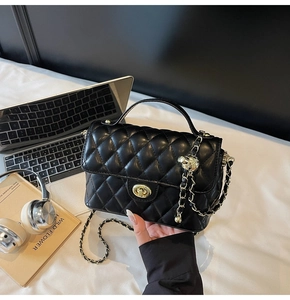 Detail of black quilted leather handbag with gold clasp and chain strap in a lifestyle setting