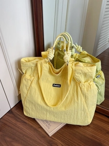 Large yellow nylon tote bag with drawstring sides and knot handle in a lifestyle setting