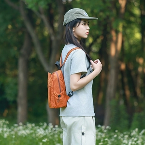 Side view of a vibrant orange nylon backpack on a model in a natural outdoor forest setting