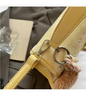 Detail of light yellow handbag with silver hardware and plush ball charm accessory