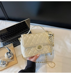 Detail of cream quilted handbag featuring gold metal turn-lock and chain strap