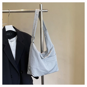 Detail of light gray nylon crescent tote bag hanging next to a black blazer