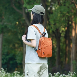 Detail of a lightweight orange nylon mini backpack worn outdoors with adjustable straps