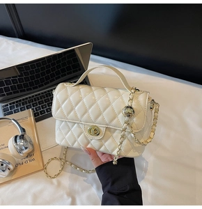 Detail of cream quilted handbag with gold metal twist lock and chain strap on desk