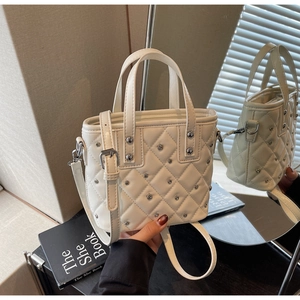 Detail der cremefarbenen Stepptasche mit silbernen Metallnieten auf Reflexfläche