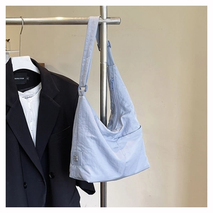 Detail of light blue nylon tote bag with silver clover charm and adjustable strap on hanger