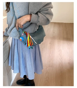 Detail of crescent moon shoulder bag with colorful woven tassels and blue cartoon keychain