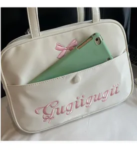 Detail of a beige PU tote bag featuring pink bow embroidery and a tablet in the front pocket