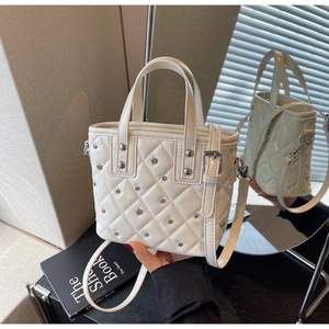 Nahaufnahme der cremefarbenen Stepptasche mit silbernen Nieten und Spiegelung