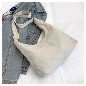 Detail of light grey nylon dumpling bag with adjustable strap on denim jacket