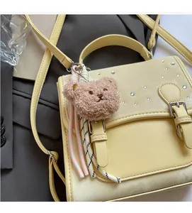 Detail view of yellow crossbody bag with rhinestone flap and plush bear charm accessory