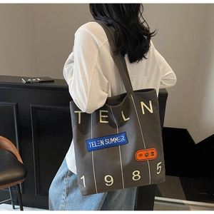 Detail of grey canvas tote bag featuring graphic letter prints and adjustable shoulder strap