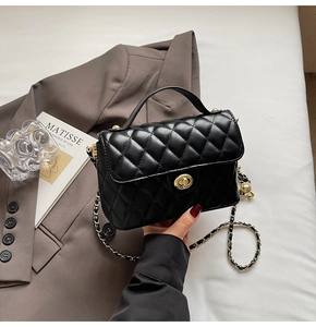 Detail of black quilted leather handbag with gold twist lock and chain strap on blazer