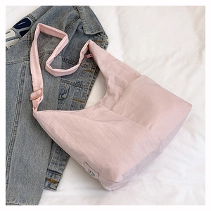 Detailed shot of pink nylon tote bag with adjustable strap on white bedding