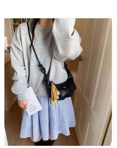 Detail of black crescent crossbody bag with colorful woven tassel and cartoon patch