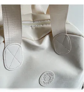 Detailansicht einer beigen Nylontasche mit verstärkten Nähten und rundem Logo-Detail