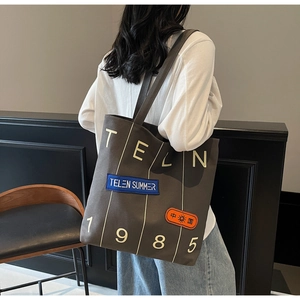 Detail of dark grey canvas tote bag featuring white TELN 1985 print and vintage patches