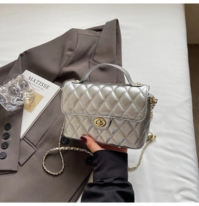 Detail of silver quilted crossbody bag featuring a golden twist lock and chain strap