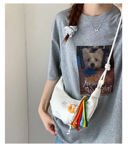 Detail of white half-moon crossbody bag featuring colorful tassels and donut pendant