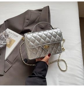 Detail of silver quilted handbag with golden twist lock and metal chain on white background