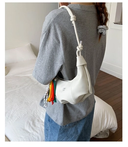 Detail of white moon bag with knot strap and colorful woven rope charm on shoulder