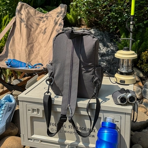 Detail of dark gray outdoor crossbody backpack on a camping box in a nature setting