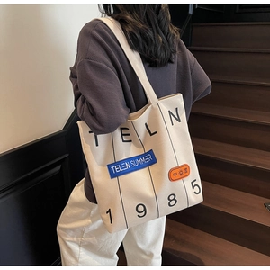 Detail of beige canvas tote bag with black stripes and embroidered TELN patches