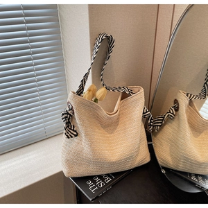 Detail of bohemian straw tote bag featuring woven texture and striped shoulder strap