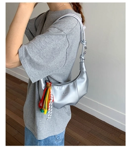 Detail of silver metallic crescent bag with knotted strap and colorful braided tassels