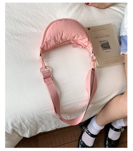 Sac bandoulière demi-lune en nylon rose sur lit blanc avec accessoires lifestyle