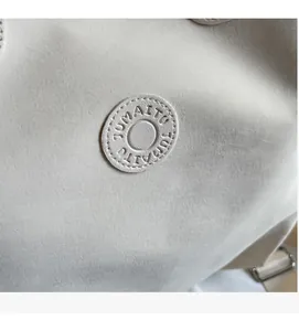 Makroaufnahme der beigen Handtasche mit JUMAITU Logo-Emblem und feinen Nähten