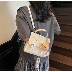 Close-up of white PU leather handbag with rhinestones and cute brown bear charm detail