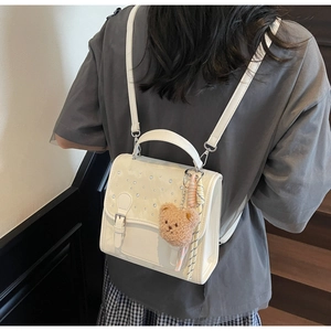 Detail view of a cream mini backpack featuring a rhinestone flap and cute brown bear charm