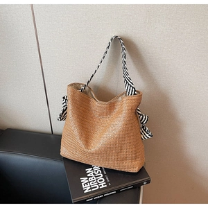 Close-up of woven straw tote bag featuring black and white striped ribbon handles